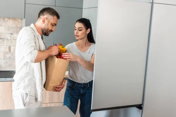 Casal colocando legumes frescos na geladeira na cozinha em casa — Fotografia de Stock