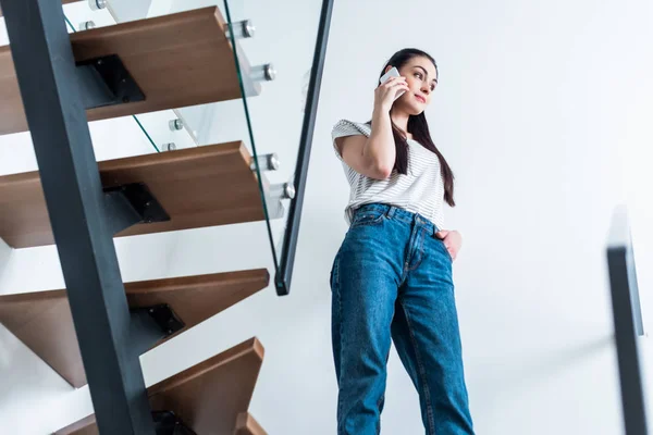 Visão de baixo ângulo da mulher atraente falando no smartphone enquanto está de pé em escadas em casa — Fotografia de Stock