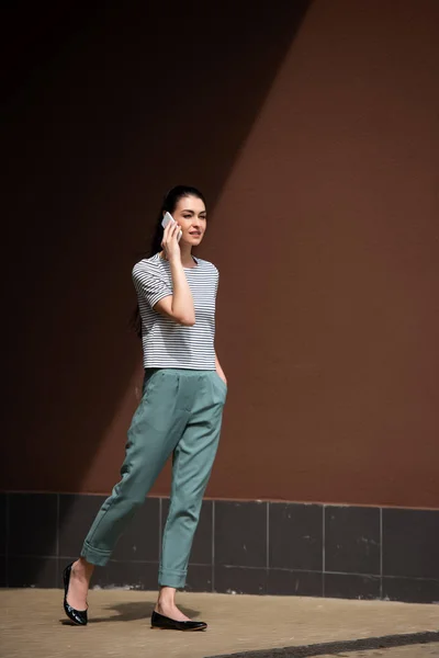 Mujer elegante caminando en la calle y hablando en el teléfono inteligente - foto de stock