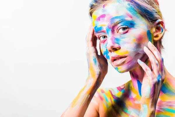 Menina atraente com colorido corpo brilhante arte tocando rosto e olhando para a câmera isolada no branco — Fotografia de Stock