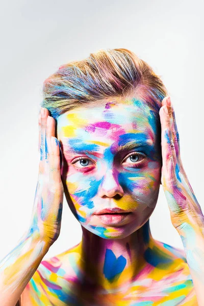 Menina atraente com colorido brilhante corpo arte tocando cabeça e olhando para a câmera isolada no branco — Fotografia de Stock