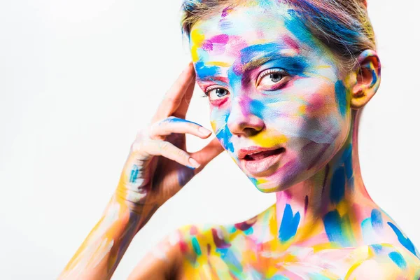Attraente ragazza con colorata brillante corpo arte toccare la testa e guardando la fotocamera isolata su bianco — Foto stock