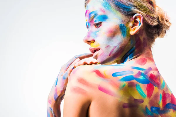 Vista lateral de chica atractiva con colorido arte del cuerpo brillante tocando labio aislado en blanco - foto de stock