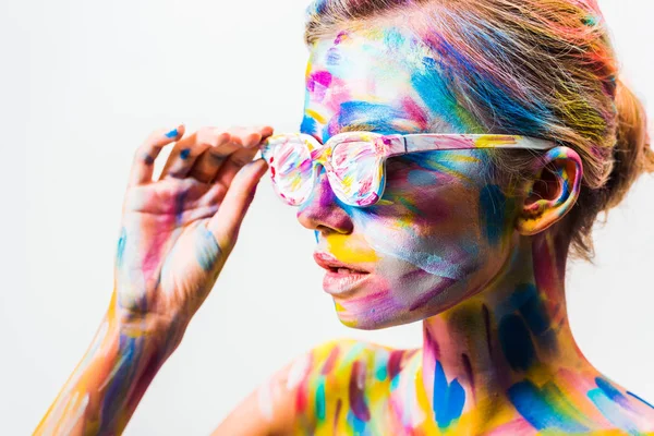 Attraente ragazza con colorato brillante arte del corpo toccando occhiali da sole isolati su bianco — Foto stock