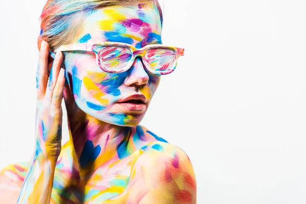 Attraente ragazza con colorata arte del corpo luminoso e occhiali da sole guardando lontano isolato su bianco — Foto stock