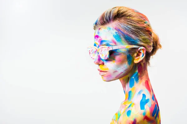 Vista lateral de chica atractiva con colorido arte corporal brillante y gafas de sol aisladas en blanco - foto de stock