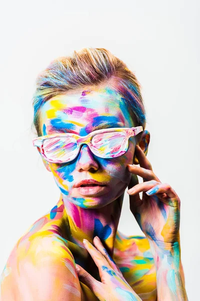 Atractiva chica con colorido brillante cuerpo arte y gafas de sol tocándose aislado en blanco - foto de stock