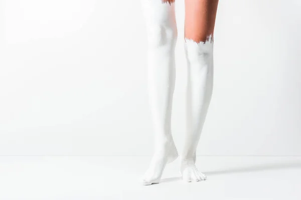 Image recadrée de fille avec des jambes peintes avec de la peinture blanche debout sur blanc — Photo de stock