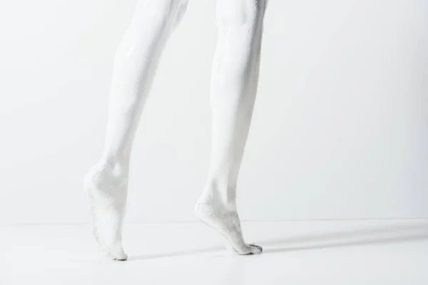 Imagen recortada de niña con las piernas pintadas con pintura blanca caminando sobre el suelo blanco - foto de stock