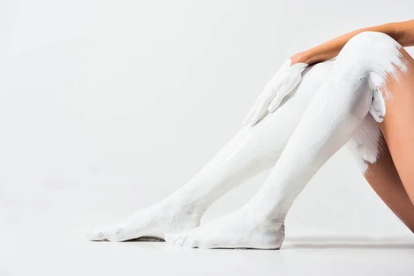 Cropped image of girl with legs and hand painted with white paint sitting on floor — Stock Photo