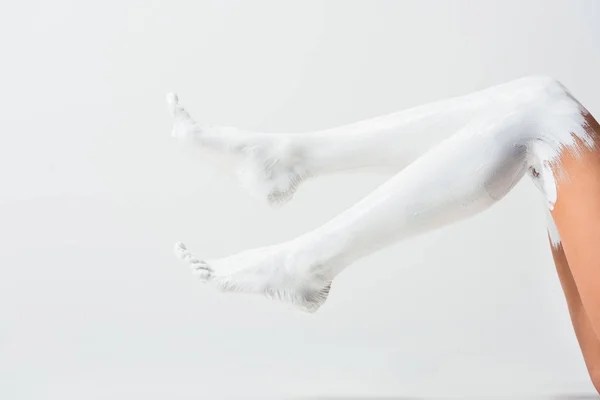 Imagen recortada de niña con las piernas pintadas con pintura blanca tumbado en el suelo aislado en blanco - foto de stock
