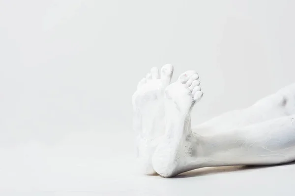 Abgeschnittenes Bild einer Frau mit mit mit weißer Farbe bemalten Beinen, die auf dem Boden liegend auf weißer Erde liegt — Stockfoto