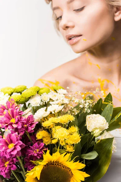 Atractiva mujer con ramo de flores y pintura amarilla en el cuerpo aislado en blanco - foto de stock