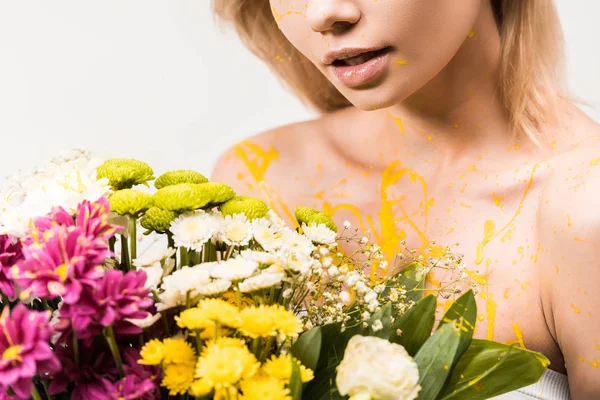 Imagen recortada de mujer con pintura amarilla en el cuerpo sosteniendo ramo de flores aisladas en blanco - foto de stock