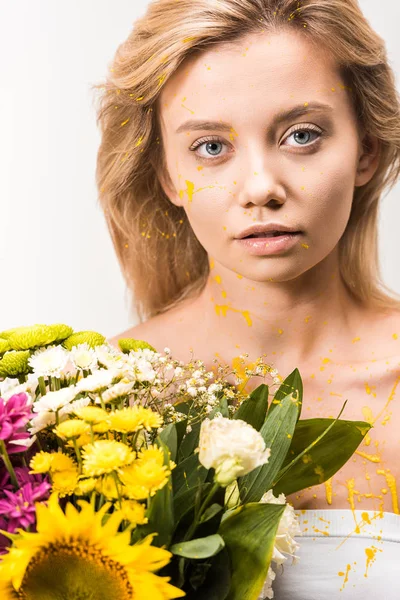 Atractiva mujer con pintura amarilla en el cuerpo sosteniendo ramo de flores y mirando a la cámara aislada en blanco - foto de stock