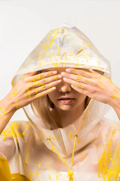 Frau im Regenmantel mit gelber Farbe bemalt, die Augen bedeckt, die Hände isoliert auf weiß — Stockfoto