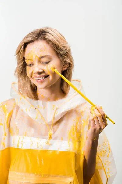 Belle femme en imperméable peinture visage avec de la peinture jaune et regardant vers le bas isolé sur blanc — Photo de stock