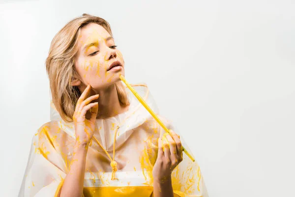 Beautiful woman in raincoat painting face with yellow paint isolated on white — Stock Photo
