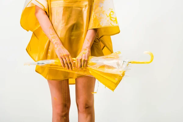 Image recadrée de femme en imperméable peint avec de la peinture jaune tenant parapluie isolé sur blanc — Photo de stock