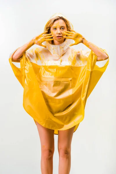 Belle femme en imperméable peint avec de la peinture jaune montrant les mains peintes isolées sur blanc — Photo de stock