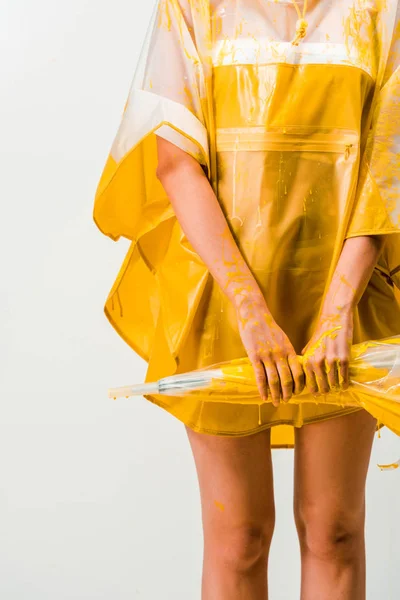 Imagen recortada de la mujer en impermeable pintado con pintura amarilla que sostiene el paraguas aislado en blanco - foto de stock