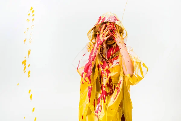 Mujer en impermeable pintado con pinturas amarillas y rojas que protegen la cara de pinturas aisladas en blanco - foto de stock