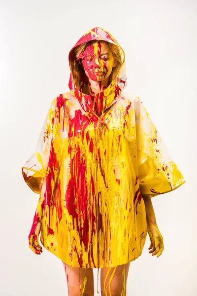 Hermosa mujer en impermeable pintado con pinturas amarillas y rojas de pie con los ojos cerrados aislados en blanco - foto de stock