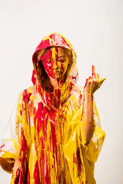 Mädchen im Regenmantel bemalt mit gelben und roten Farben, die den Mittelfinger isoliert auf weiß zeigen — Stockfoto