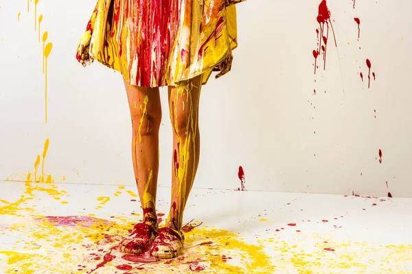 Imagen recortada de la mujer pintada con pinturas amarillas y rojas de pie en el suelo - foto de stock