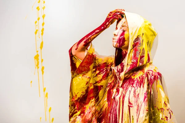 Вид збоку жінки в плащі, пофарбованому жовтими та червоними фарбами, знімає капюшон ізольовано на білому — стокове фото