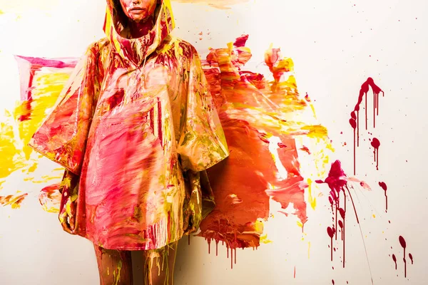 Image recadrée de la femme debout en imperméable peint avec des peintures jaunes et rouges près du mur — Photo de stock