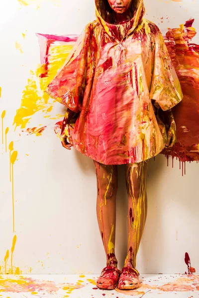 Imagen recortada de la mujer de pie en impermeable pintado con pinturas amarillas y rojas - foto de stock