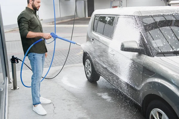 Красивий чоловік прибирає автомобіль на автомийці з струменем води високого тиску — стокове фото