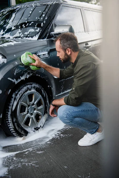 Seitenansicht eines gutaussehenden Mannes, der Auto in Waschanlage mit Lappen reinigt — Stockfoto