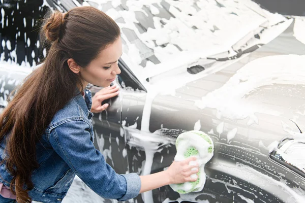 Seitenansicht der attraktiven Frau, die Auto in Waschanlage mit Lappen und Schaum reinigt — Stockfoto
