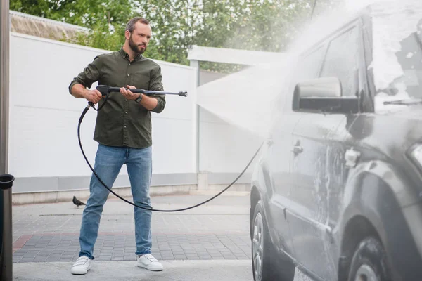 Vista laterale di bello uomo pulizia auto a lavaggio auto con getto d'acqua ad alta pressione — Foto stock