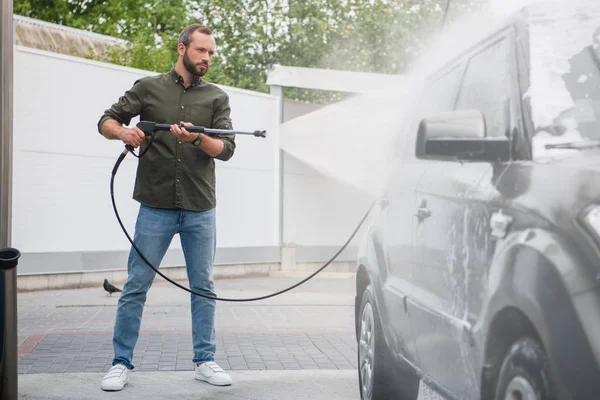 Vista lateral del hombre guapo coche de limpieza en el lavado de coches con chorro de agua de alta presión - foto de stock