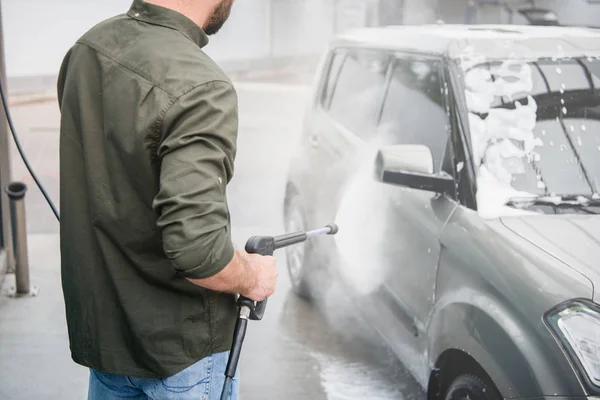 Image recadrée de l'homme nettoyage de voiture de mousse au lavage de voiture avec jet d'eau haute pression — Photo de stock