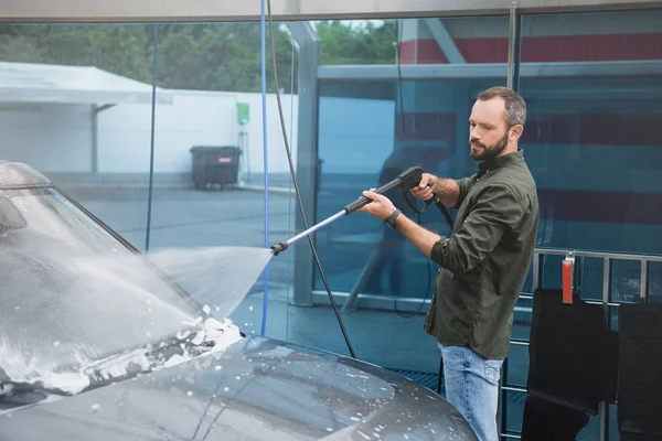 Schöner Mann reinigt Autoscheibe an Waschanlage mit Hochdruck-Wasserstrahl — Stockfoto