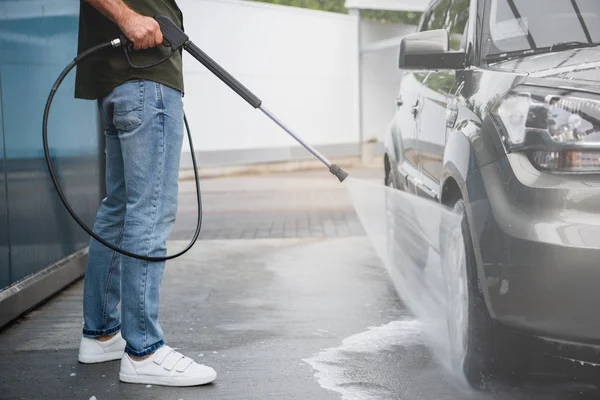 Geschnittenes Bild eines Mannes, der Auto in Waschanlage mit Hochdruck-Wasserstrahl reinigt — Stockfoto