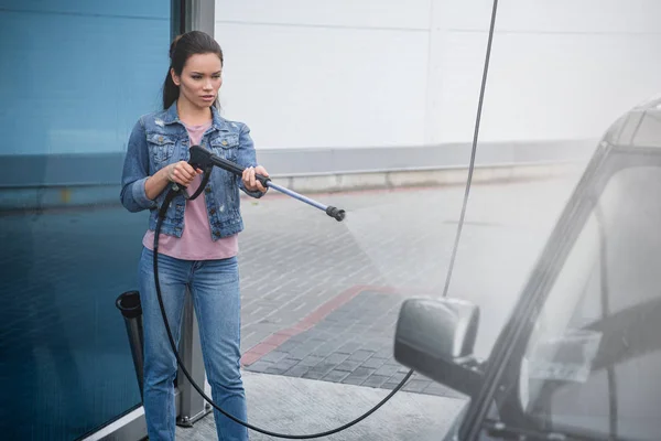 Привлекательная женщина моет машину на автомойке с водяной струей высокого давления — стоковое фото