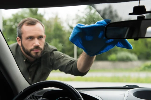 Homem bonito limpando janela do carro frontal com pano — Fotografia de Stock