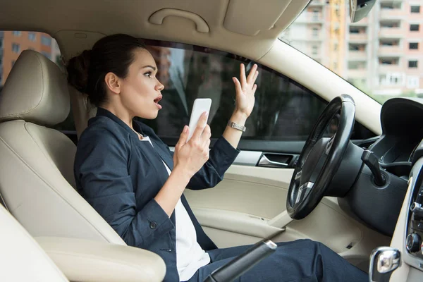 Mulher de negócios chocada segurando smartphone e olhando para longe no carro — Fotografia de Stock