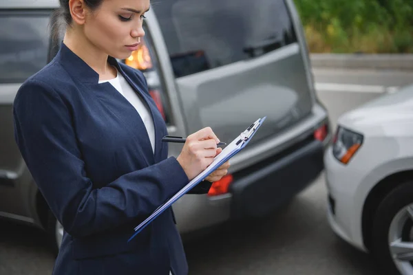 Vista laterale di donna attraente scrivere qualcosa per l'assicurazione auto dopo incidente stradale — Foto stock