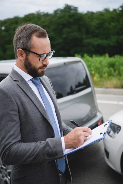 Handsome man writing something to car insurance after car accident — Stock Photo