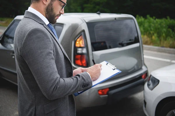 Side view of  man writing something to car insurance after car accident — Stock Photo