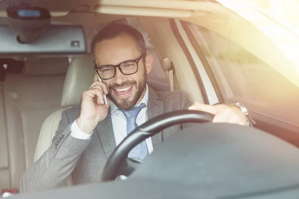 Souriant bel homme d'affaires conduisant une voiture et parlant par smartphone — Photo de stock