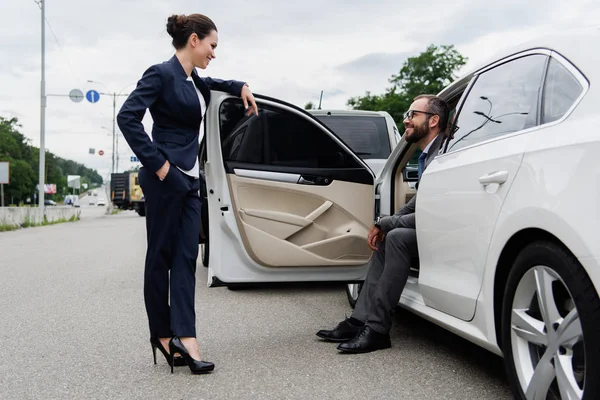 Усміхнені водії розмовляють біля машини на дорозі і дивляться один на одного — стокове фото