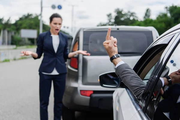 Cropped image of driver showing middle finger to businesswoman on road — Stock Photo