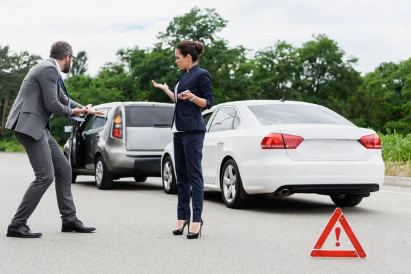 Des gens d'affaires se querellent et font des gestes sur la route après un accident de voiture — Photo de stock